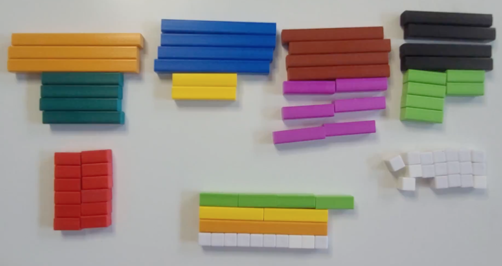 One set of cuisenaire rods. The size of rods range from 1 centimeter long to 10 centimeters longs. There are 4 orange rods representing 10, 4 blue rods representing 9, 4 brown rods representing 8, and 4 black rods representing 7. In the next row, there are 4 dark green rods representing 6, 4 yellow rods representing 5, 6 purple rods representing 4 and 10 light green rods representing 3. In the bottom row, there are 12 red rods representing a size of 2, and 28 white rods grouped into 4 rows of 7. The white rods represent size 1. In the center, 10 white rods in a row, 1 orange rod lined up to the white rods on top. 2 yellow rods stacked horizontally on top of the orange rod. 4 light green rods stacked horizontally on top of the yellow rods. The light green rods go past the ends of the other rods.